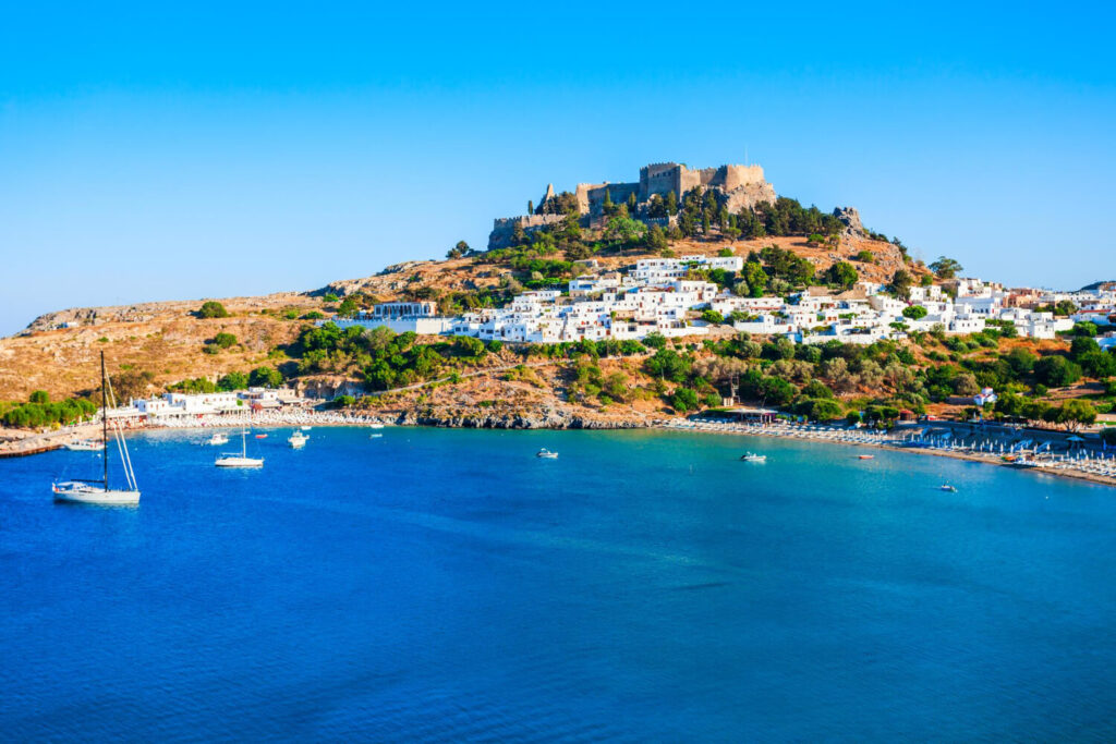 Crique paisible avec une eau turquoise et des parasols sur la plage à Rhodes, illustrant la sécurité de l'île pour les vacances.