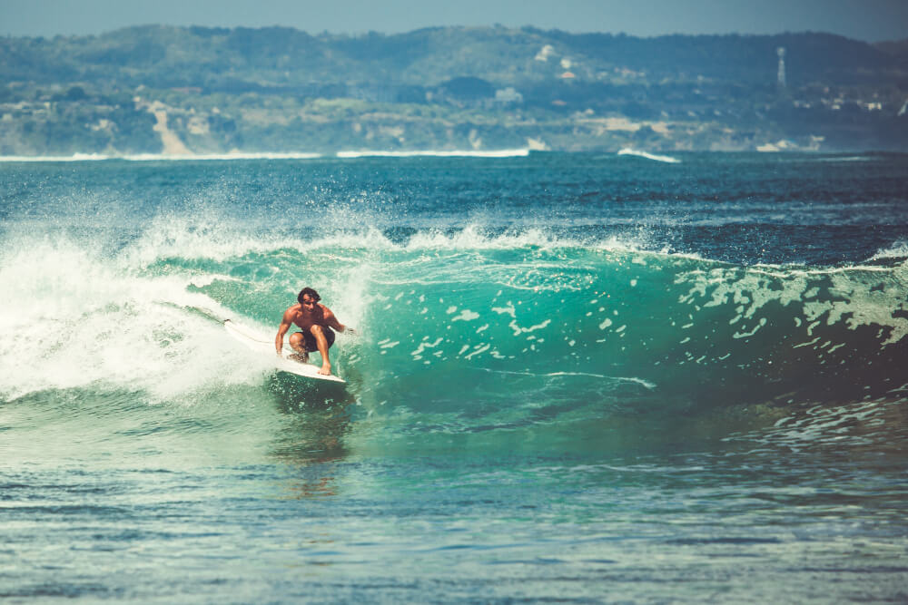 Surf à Mayotte : le guide complet des spots et des conditions 3 Surfeur ridant une vague parfaite sur un récif corallien, avec les eaux turquoise du lagon de Mayotte en arrière-plan.