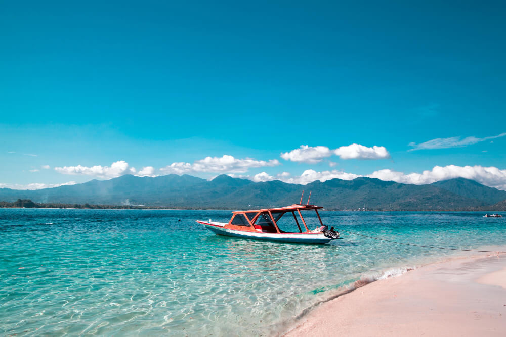 Paysage spectaculaire de Lombok avec une plage de sable blanc, des cocotiers et des collines verdoyantes en arrière-plan.
