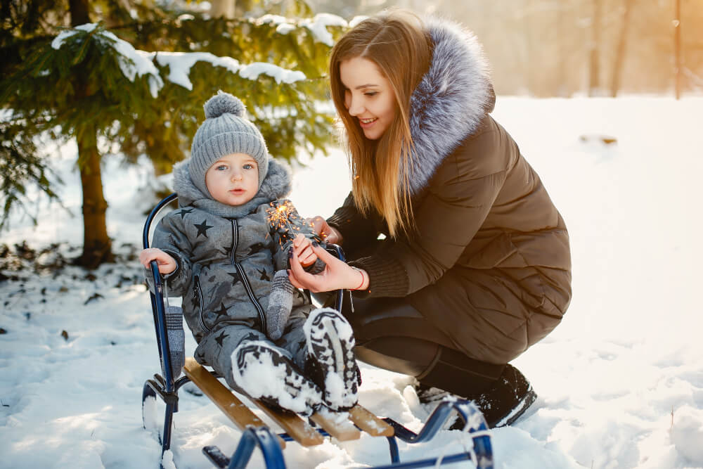 Bébé bien emmitouflé dans une poussette luge à la montagne, avec des sommets enneigés en fond.