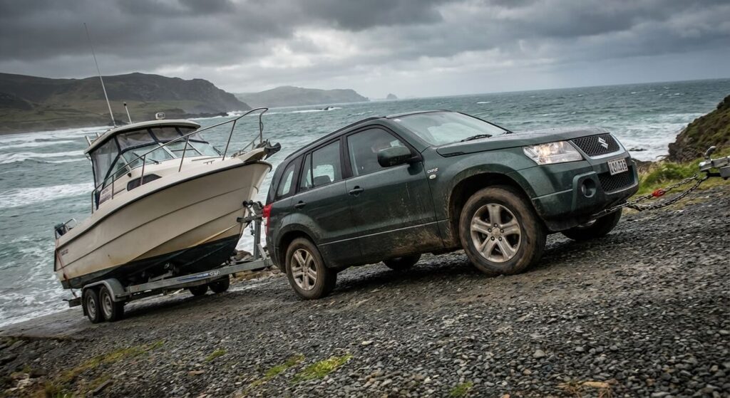 Suzuki Grand Vitara 1.9 DDiS attelé à une remorque porte-bateau, illustrant ses capacités de traction.