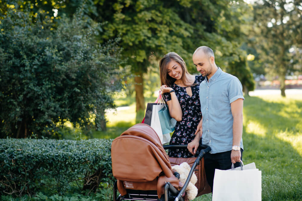 Jeunes parents souriants se promenant dans un parc ensoleillé avec leur bébé d'un mois confortablement installé dans une écharpe de portage