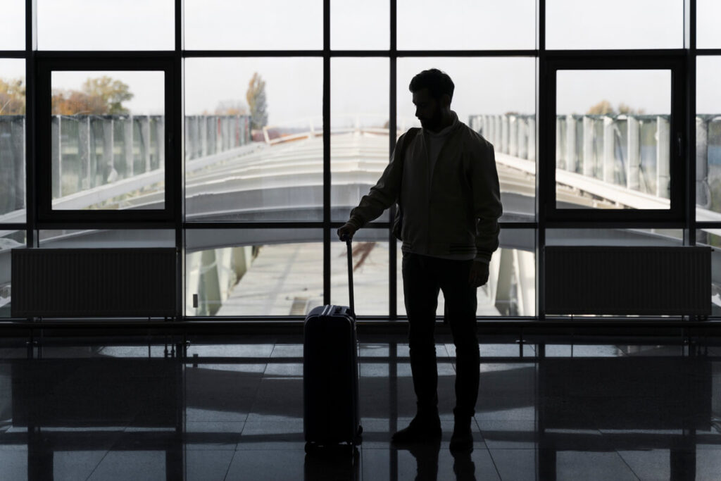 Silhouette d'une personne seule avec une valise sur le quai d'une gare attendant son train pour partir au loin.
