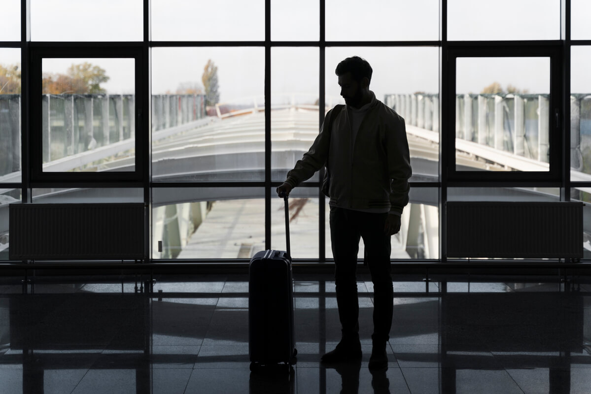 Silhouette d'une personne seule avec une valise sur le quai d'une gare attendant son train pour partir au loin.